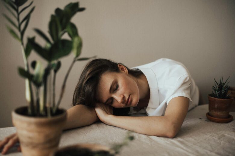 Woman is very tired, she is laying her head on a table with plants on it