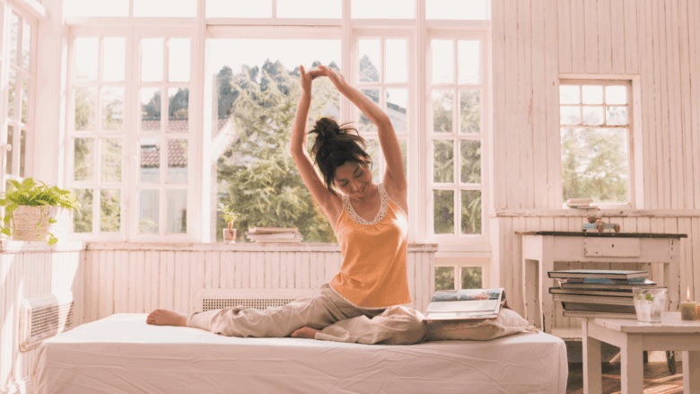 A young woman stretching in her bed while she is waking up, to get ready for the day ahead